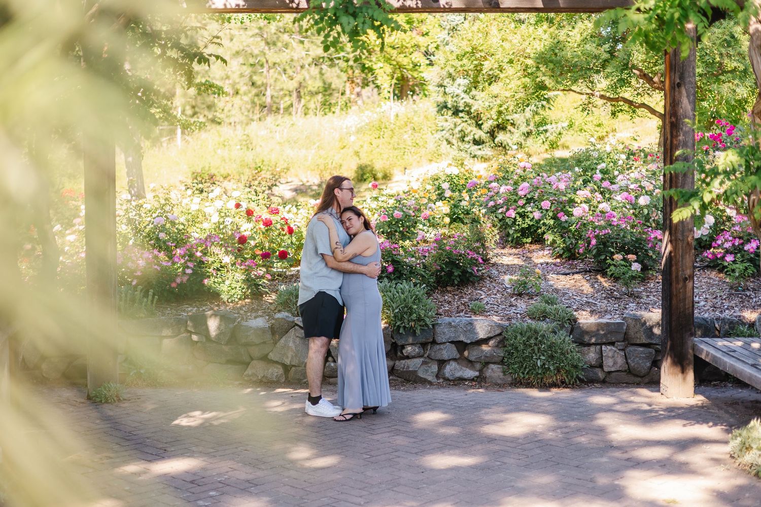 Two people embrace in a romantic moment surrounded by lush garden landscaping and natural light.
