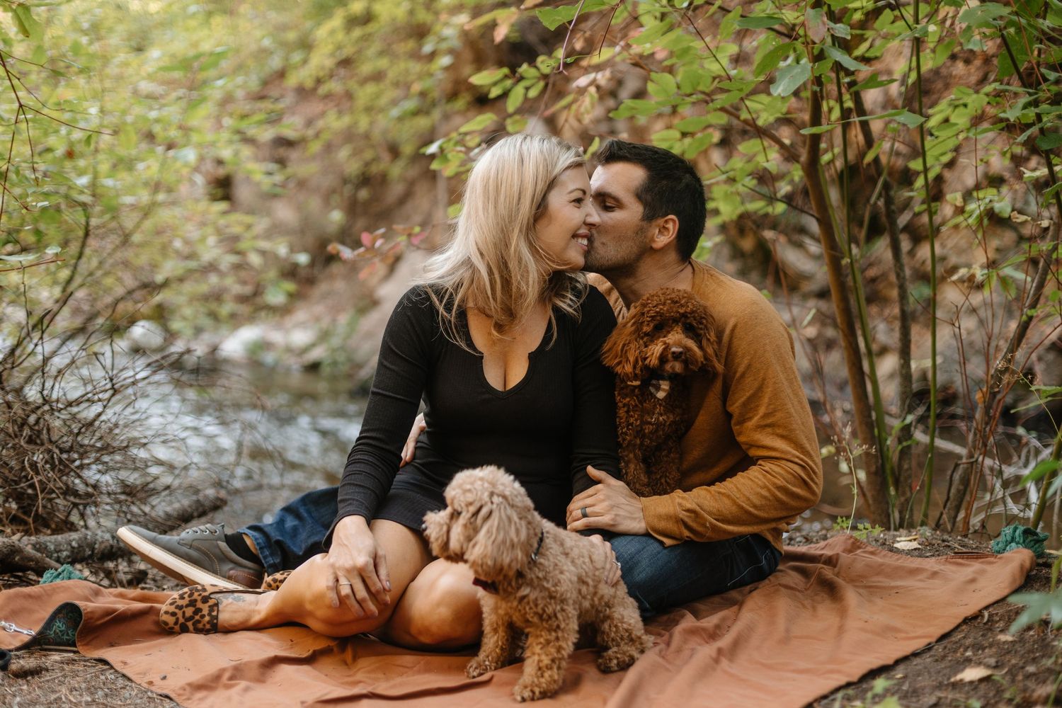 A couple and their brown poodle mix dog share tender moments in a natural outdoor setting during a photo session.