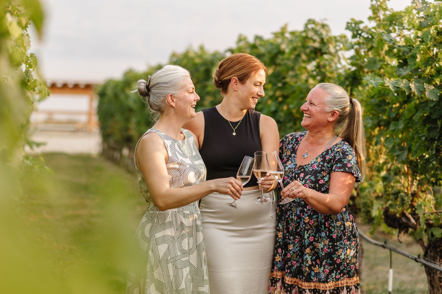 A group of people enjoying wine and conversation in a sunny vineyard setting during a summer gathering.