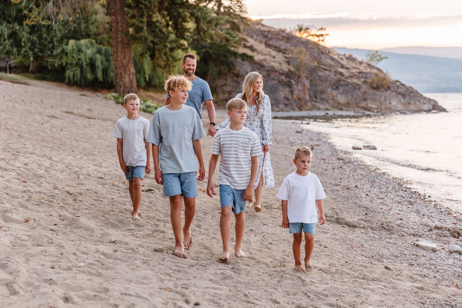 A family walking together along a scenic rocky beach coastline at sunset.