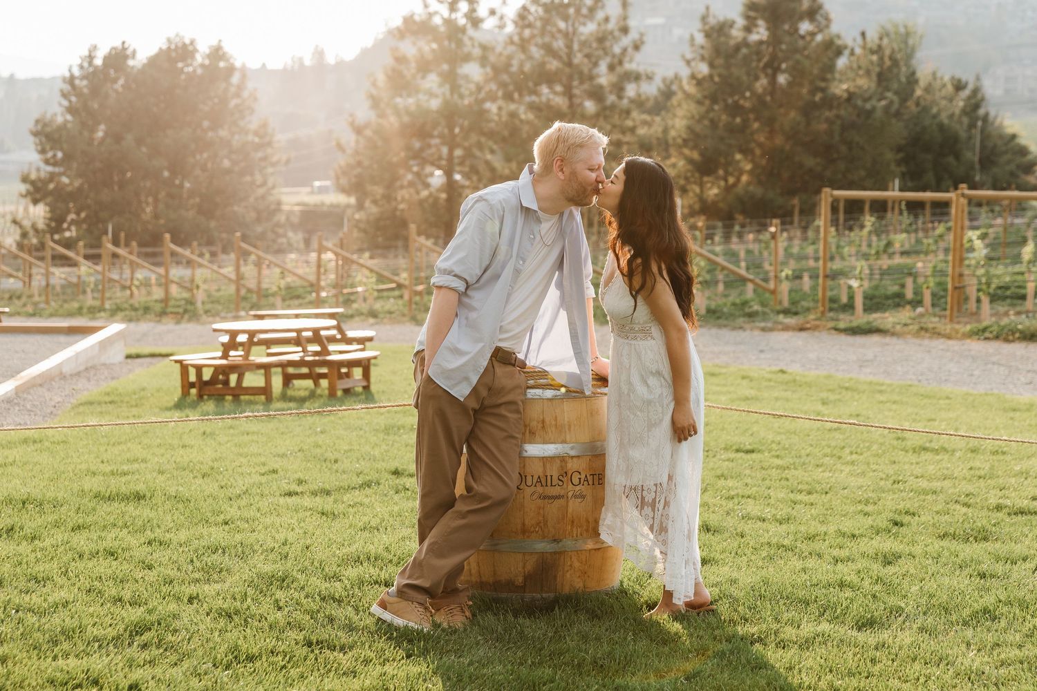A couple enjoying a romantic sunset picnic in a grassy meadow with a rustic wooden basket and blanket spread out.