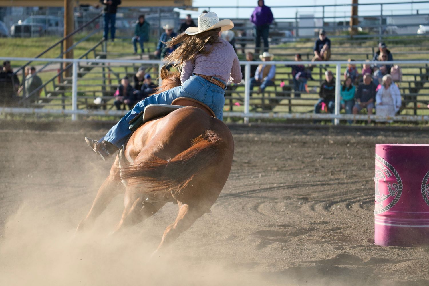 A barrel racer guides their horse at high speed around a barrel in a dusty rodeo arena during competition.