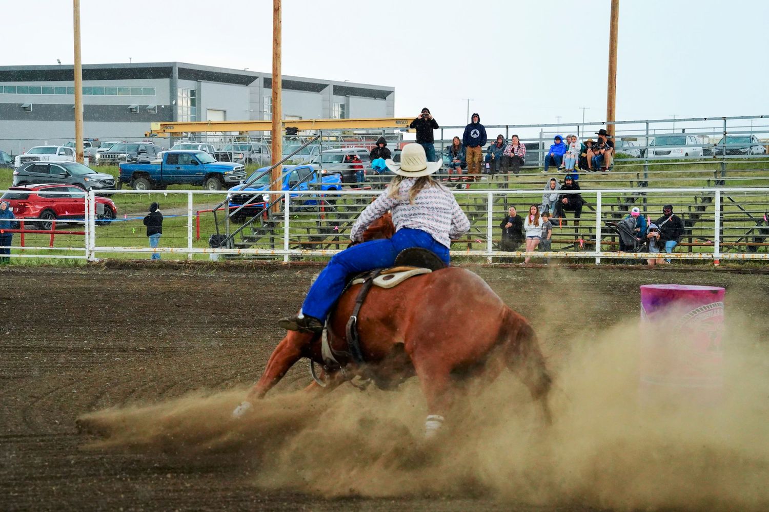 A barrel racer on horseback kicks up dust while making a sharp turn during a rodeo competition.
