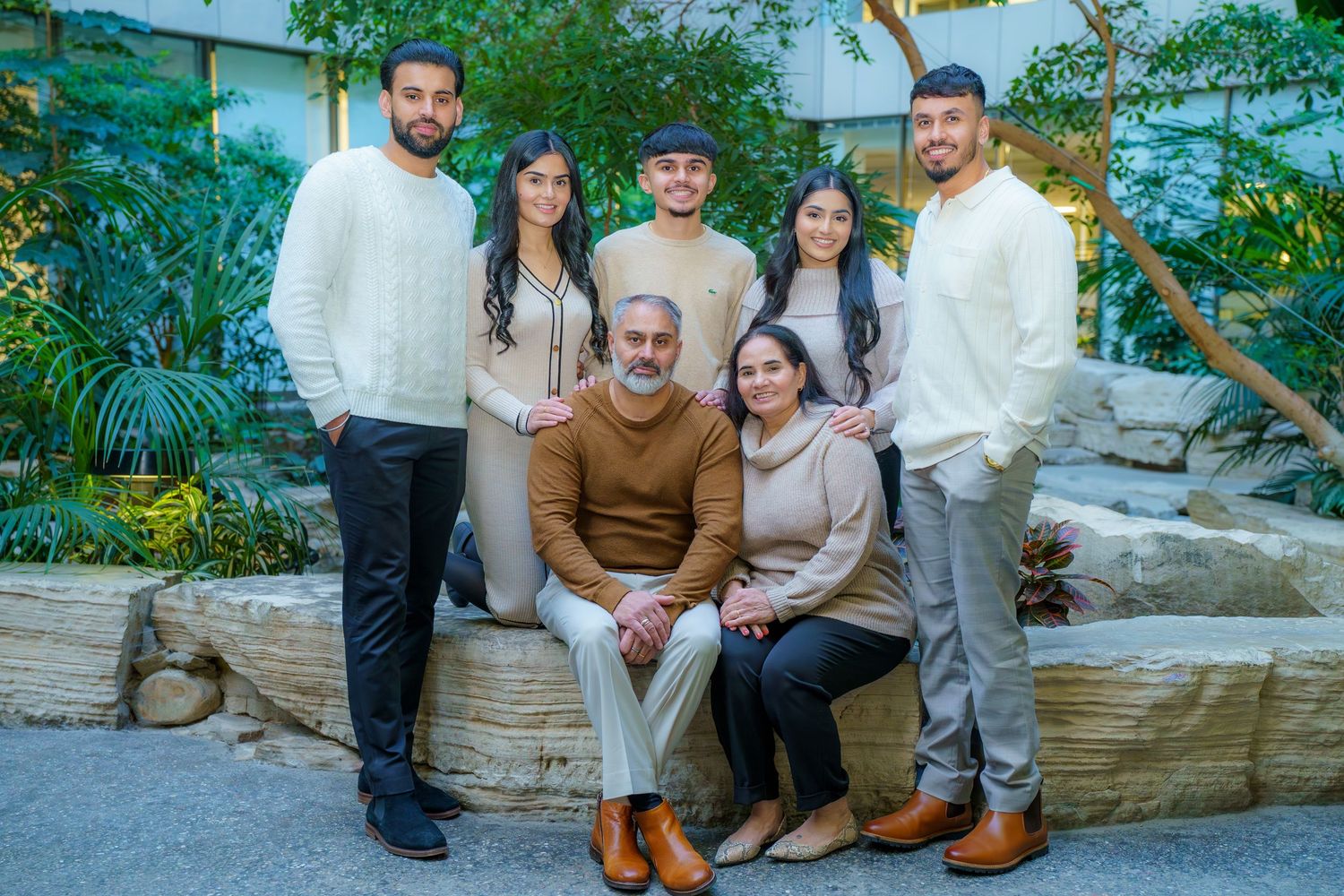 A family group poses together outdoors on stone steps surrounded by lush greenery and tropical plants in a garden setting.
