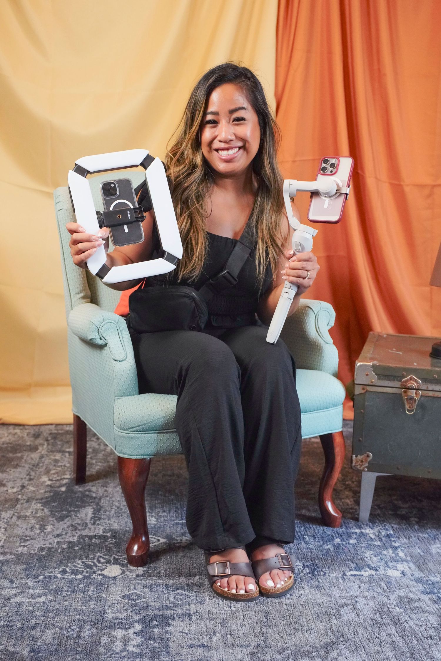 Person wearing dark clothing sits in blue armchair showcasing different views while holding white electronic devices.