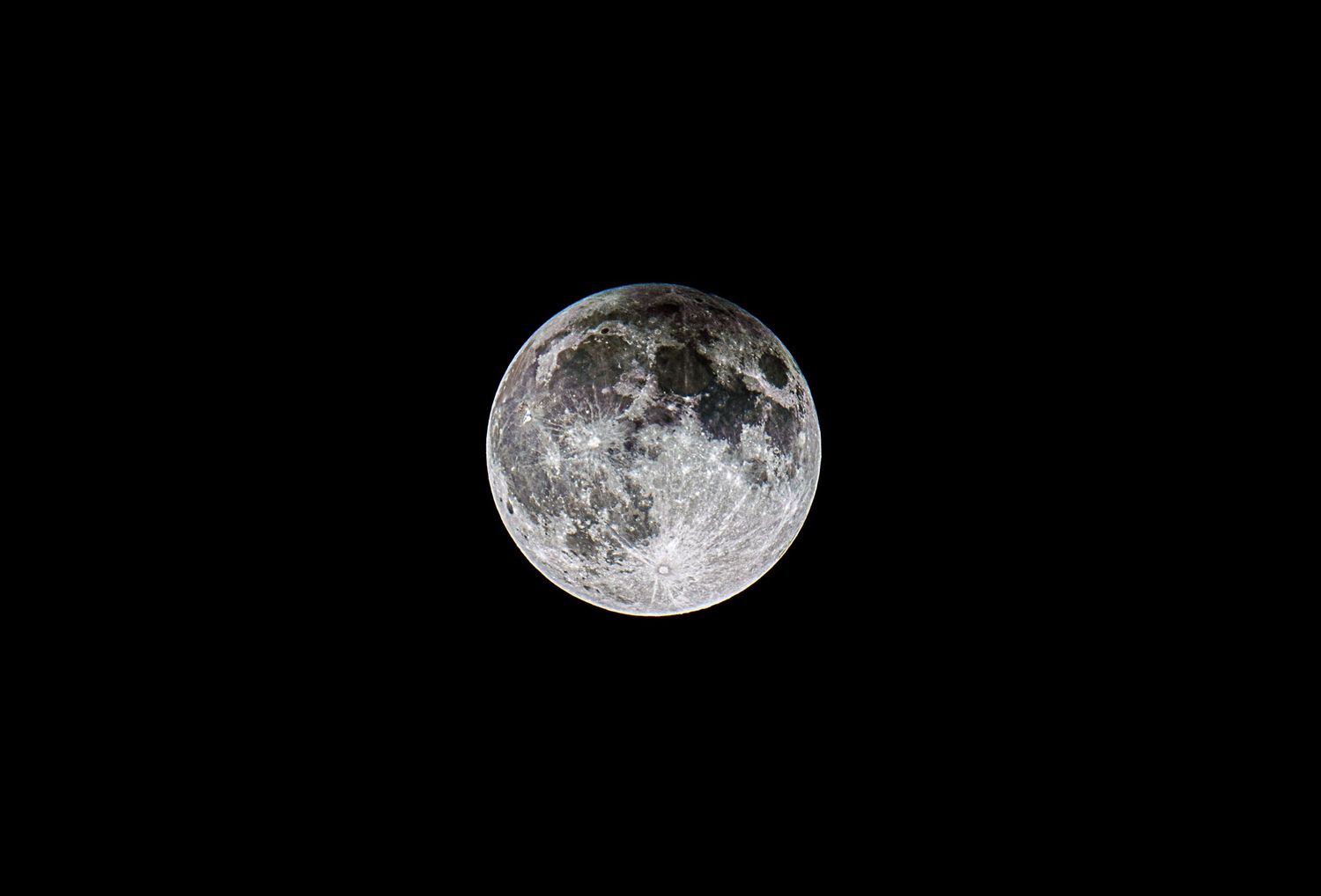 A detailed view of a full moon showing its craters and surface features against a pitch black night sky.