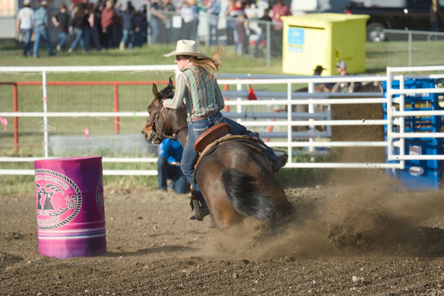 A barrel racer on horseback kicks up dust while making a tight turn around a pink barrel at a rodeo competition.