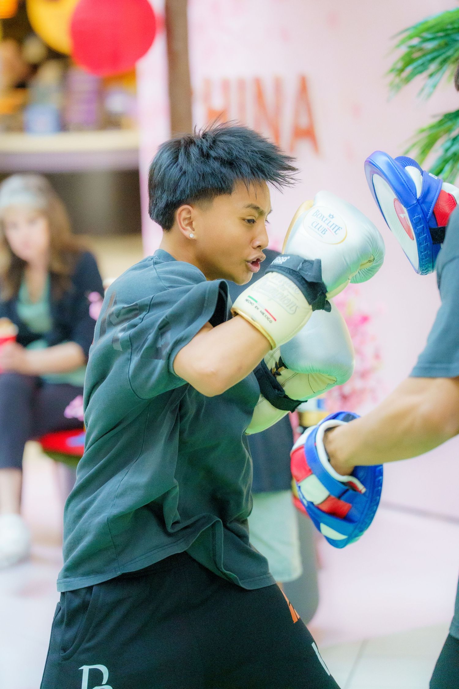 Young boxer practicing punching techniques with training mitts during an indoor workout session.