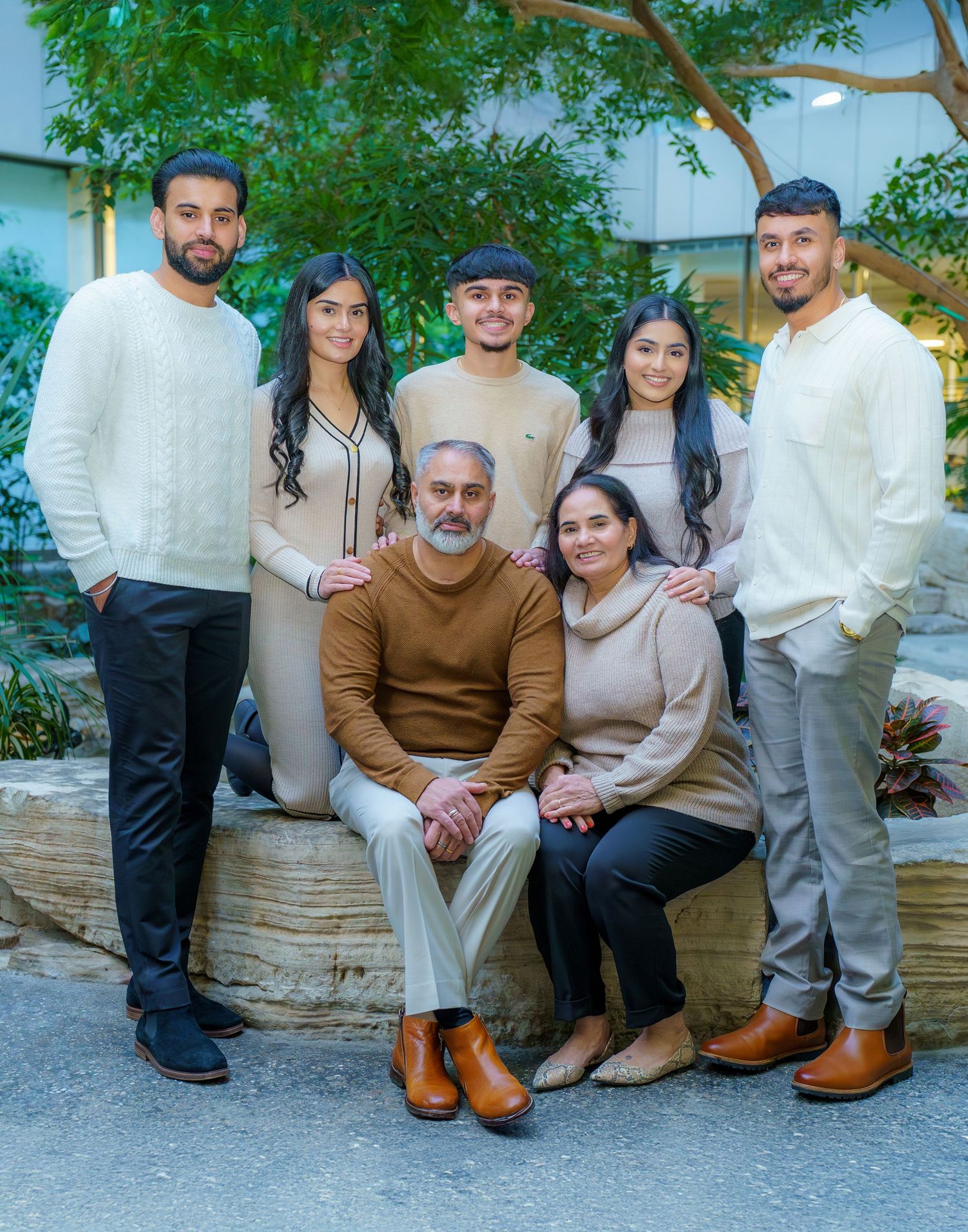 A group of people sitting on an outdoor stone bench wearing coordinated neutral-toned outfits for a casual photo.