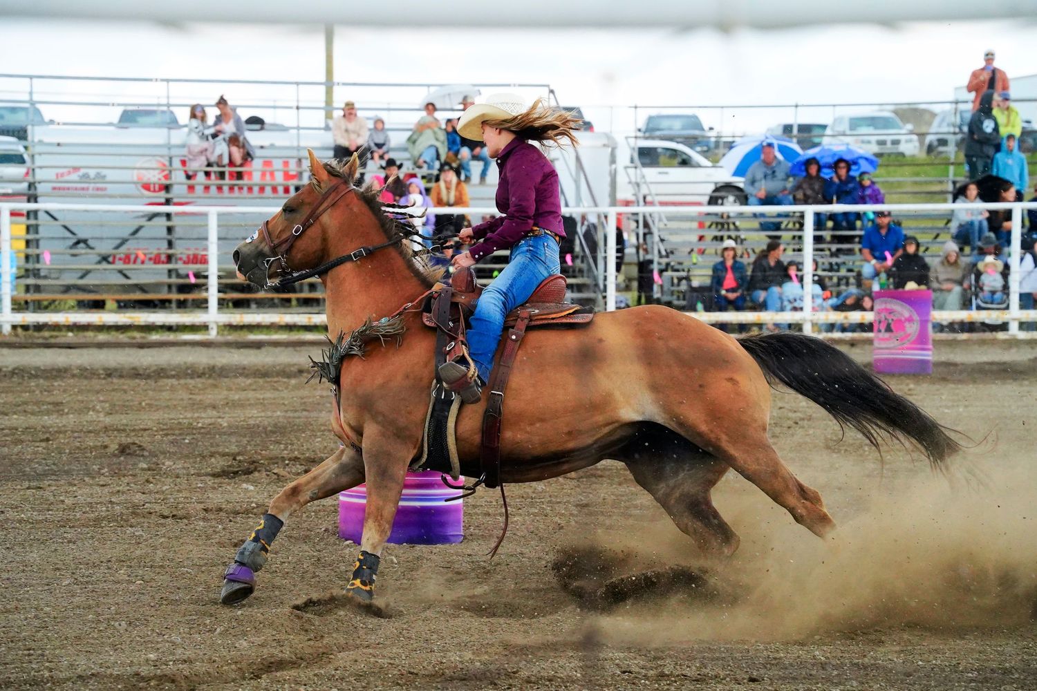 Barrel racing competitors navigate turns at high speeds during a dusty rodeo competition event.