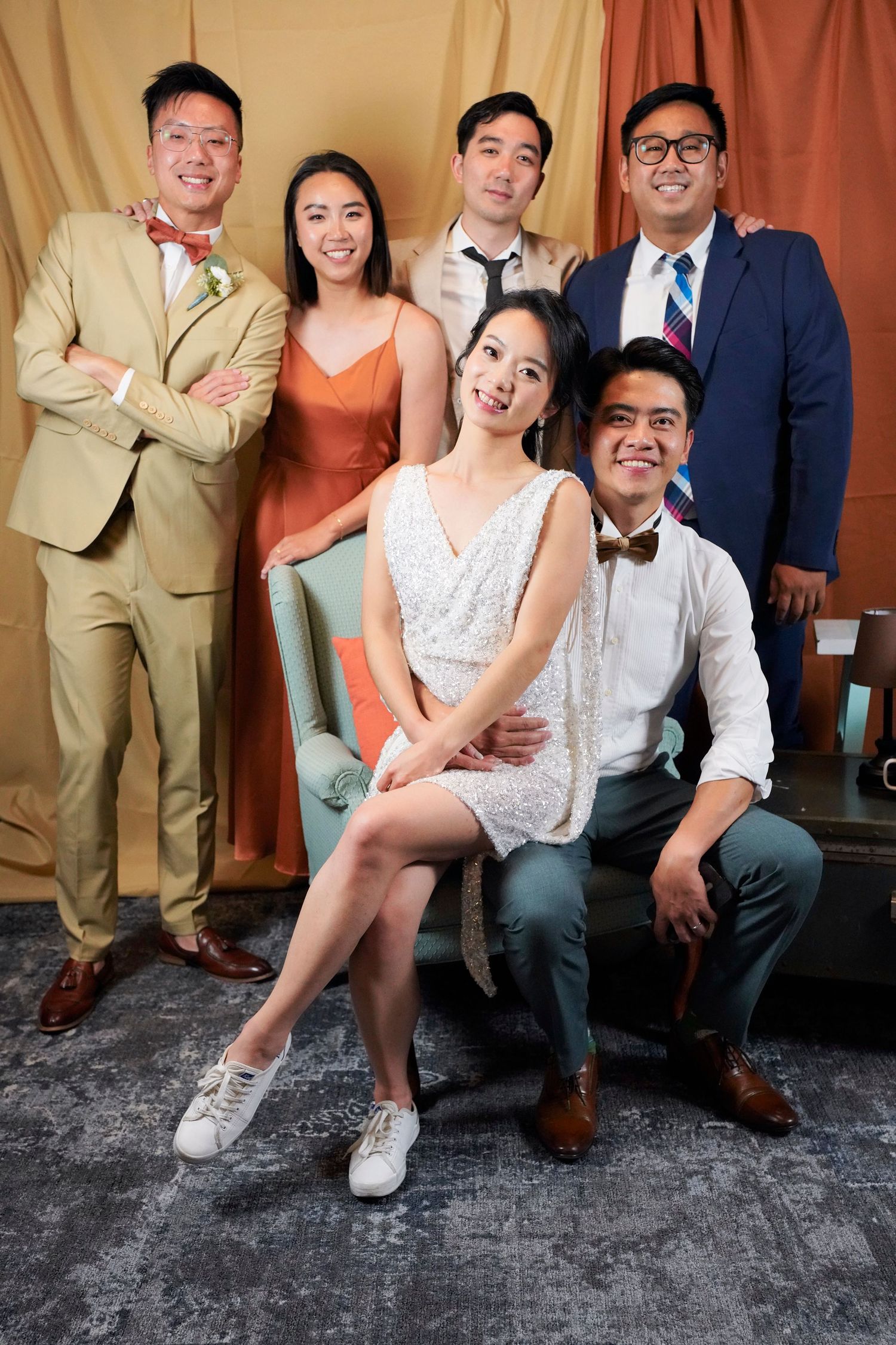A group of stylishly dressed people pose together at a formal gathering with a rustic background.
