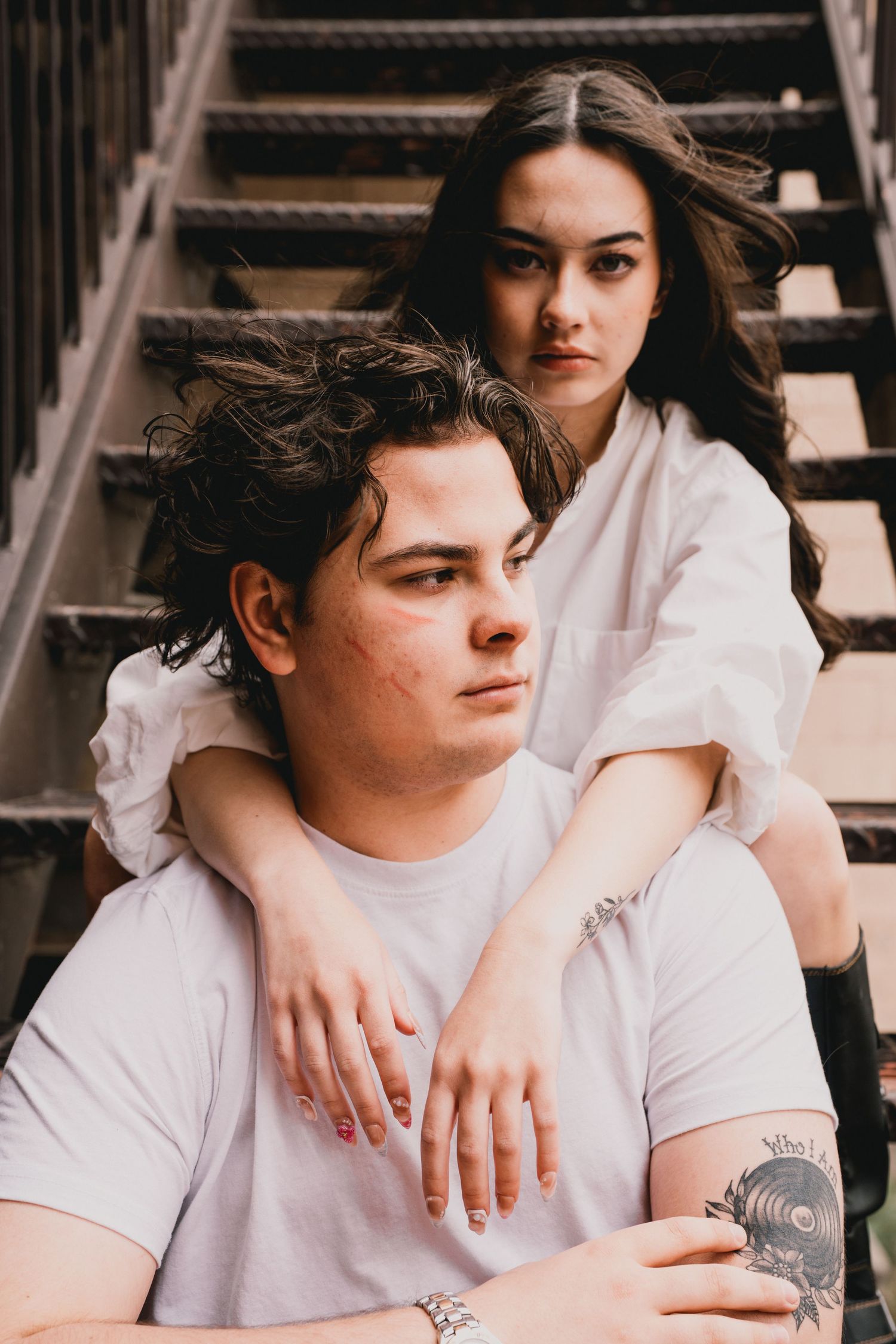 A couple in white shirts poses together on wooden stairs in a romantic vintage style photoshoot.