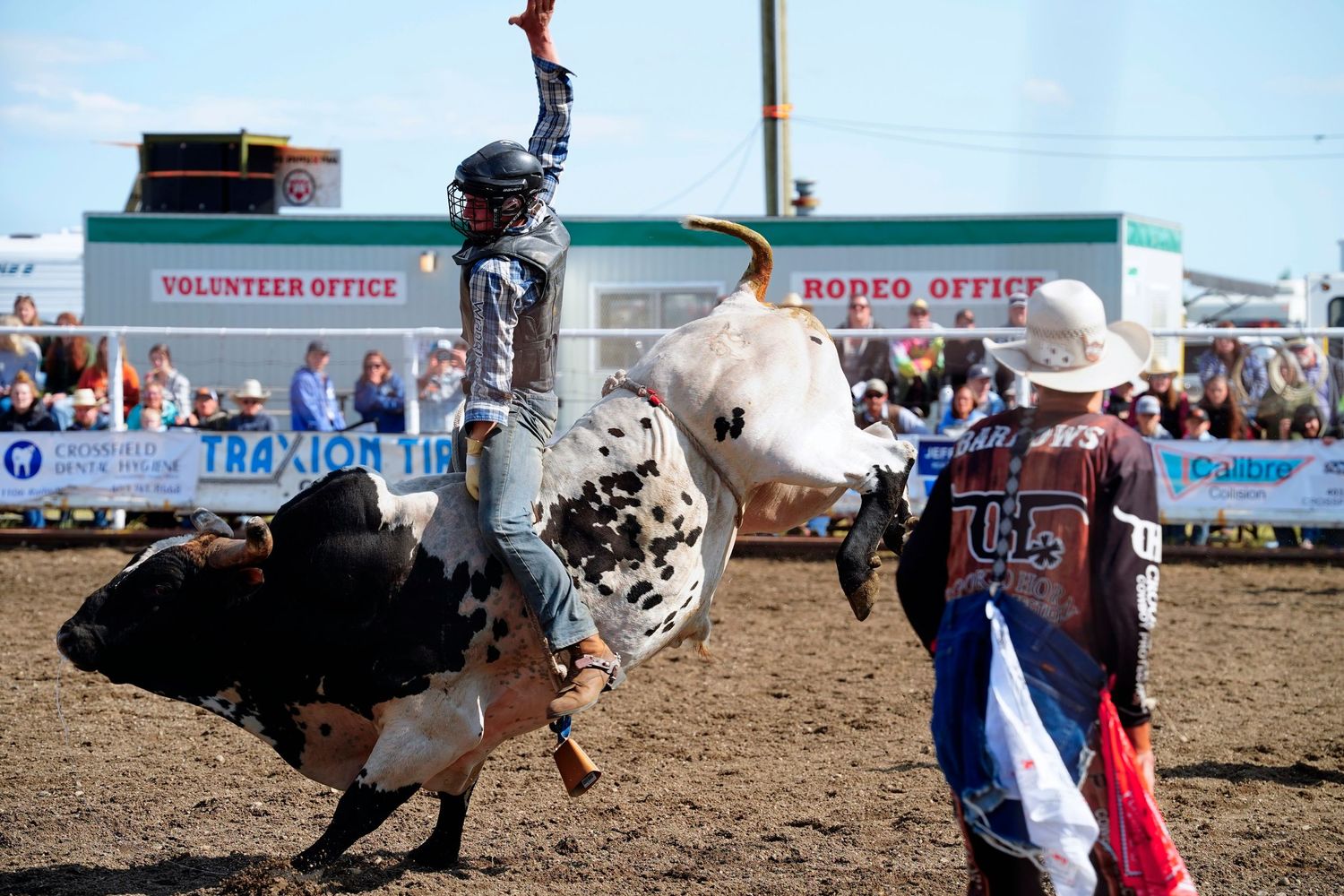 A bull rider performs during a rodeo event with spotters and observers in the arena.