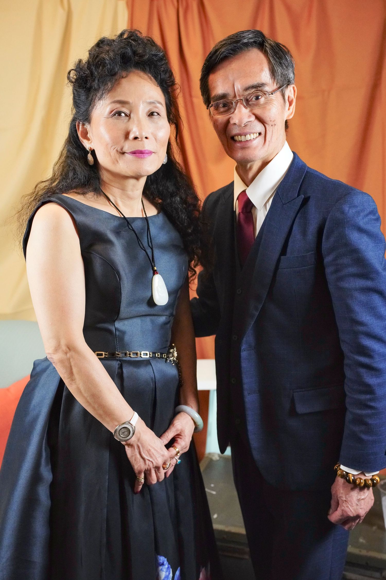 Couple in formal attire, with woman wearing black cocktail dress and man in dark suit, posing for photos at event.
