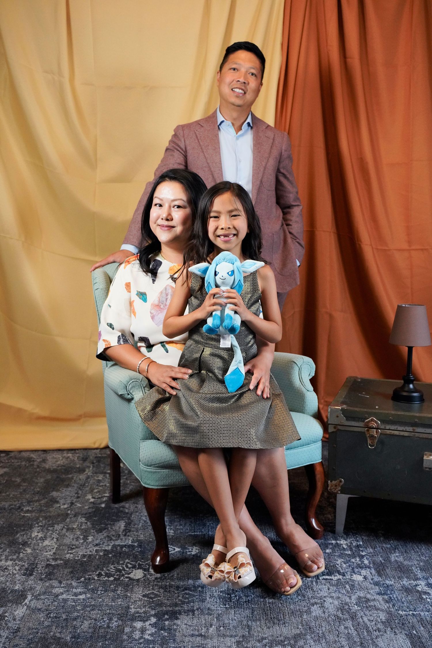 A family sits together on a bench against a brown backdrop, smiling at the camera during a professional portrait session.