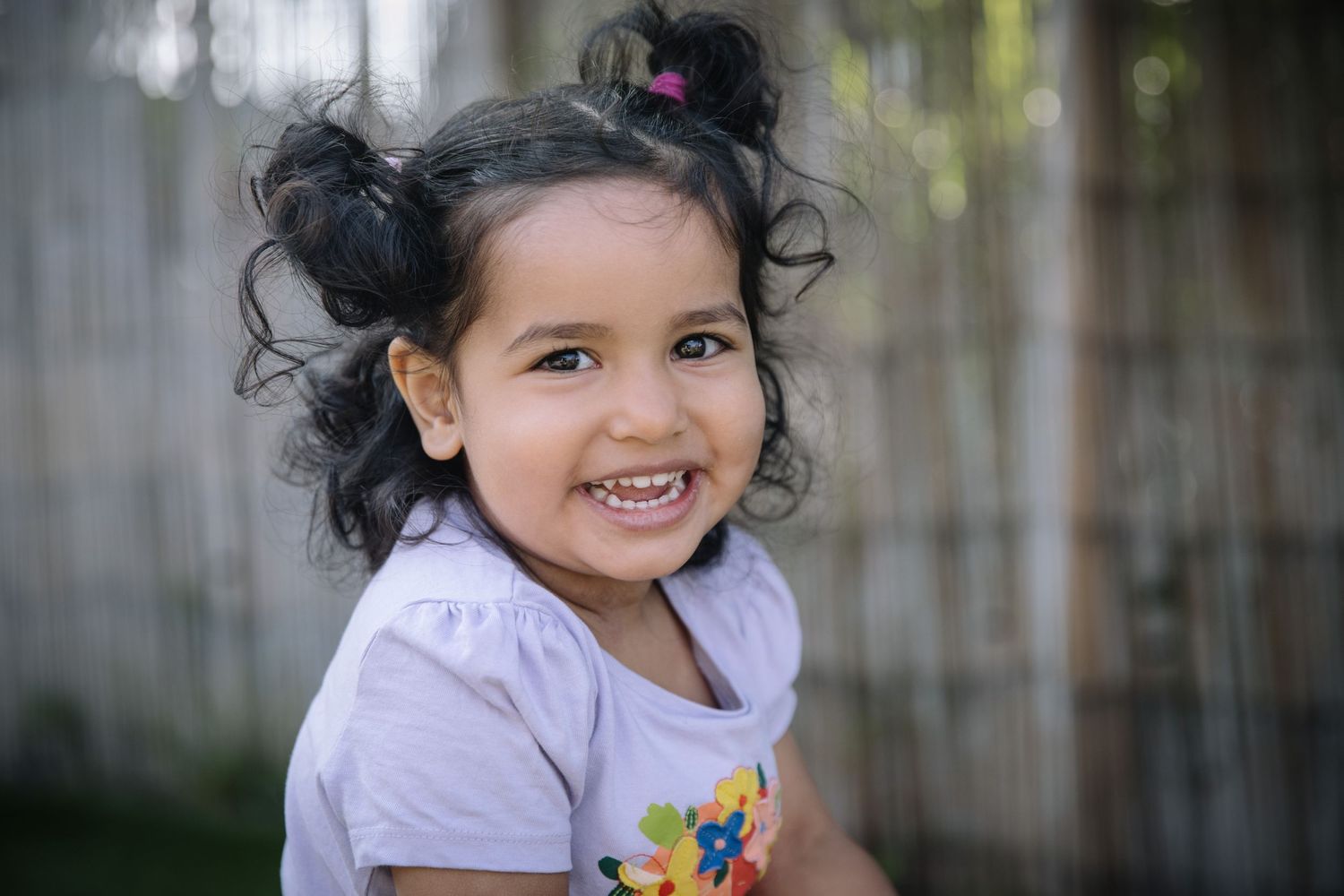 Cheerful child in a white shirt with floral detail smiles brightly.