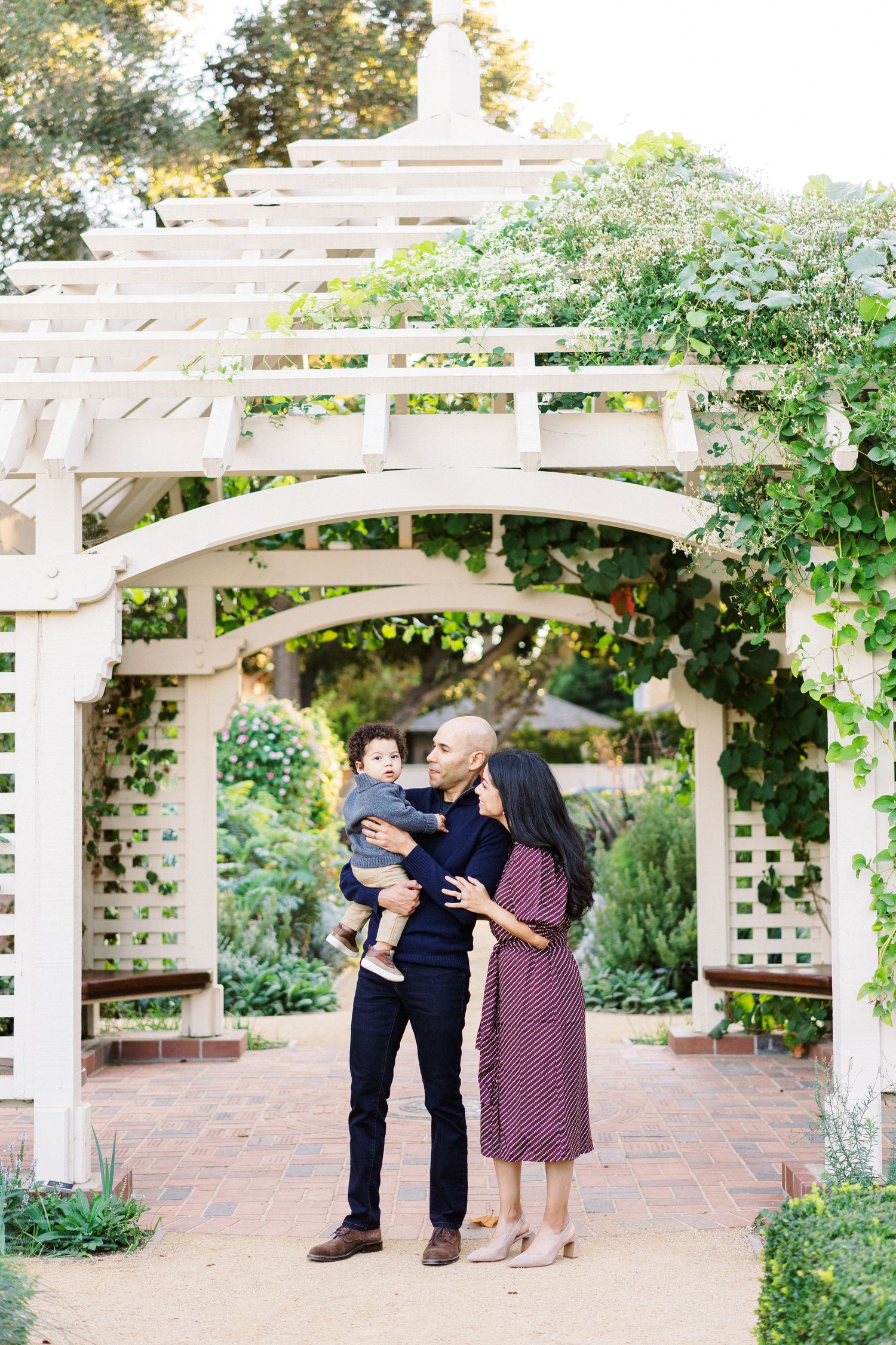 A romantic moment under a white garden pergola surrounded by lush greenery and blooming flowers.