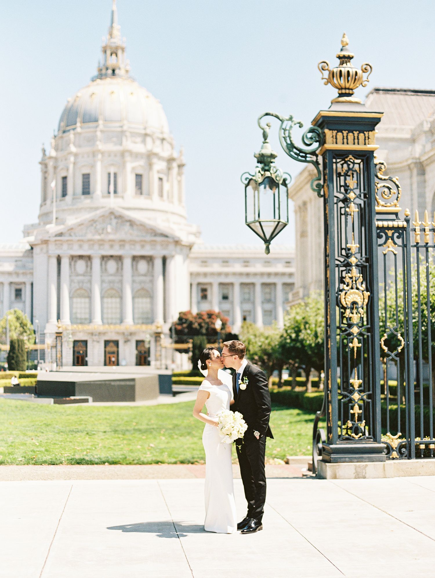 Elegant couple embraces by an ornate vintage lamppost outside San Francisco City Hall on a bright sunny day.