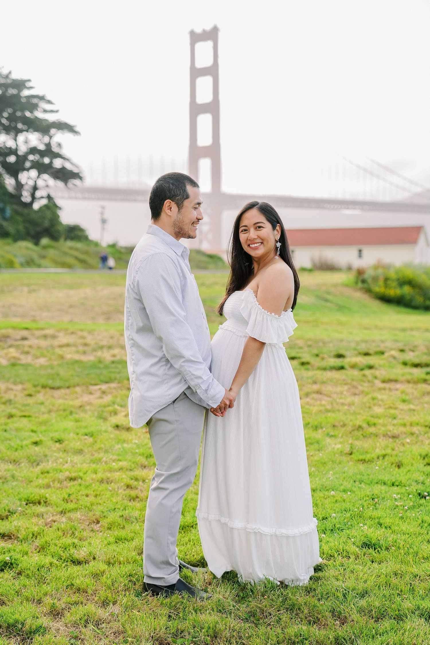 A couple shares a romantic moment on a grassy hill with the iconic Golden Gate Bridge visible in the background.