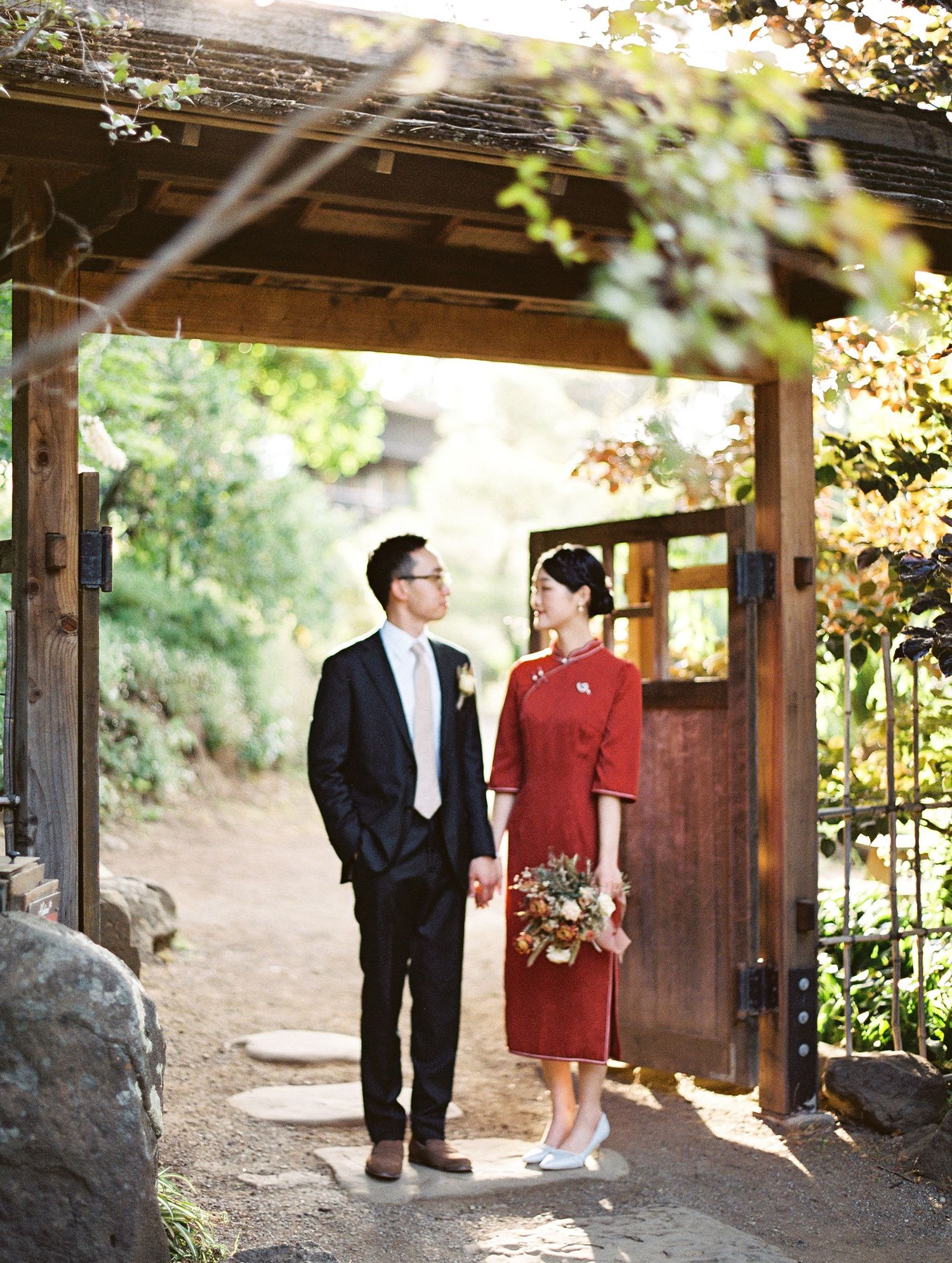 A couple poses in formalwear under a wooden archway on a garden path.