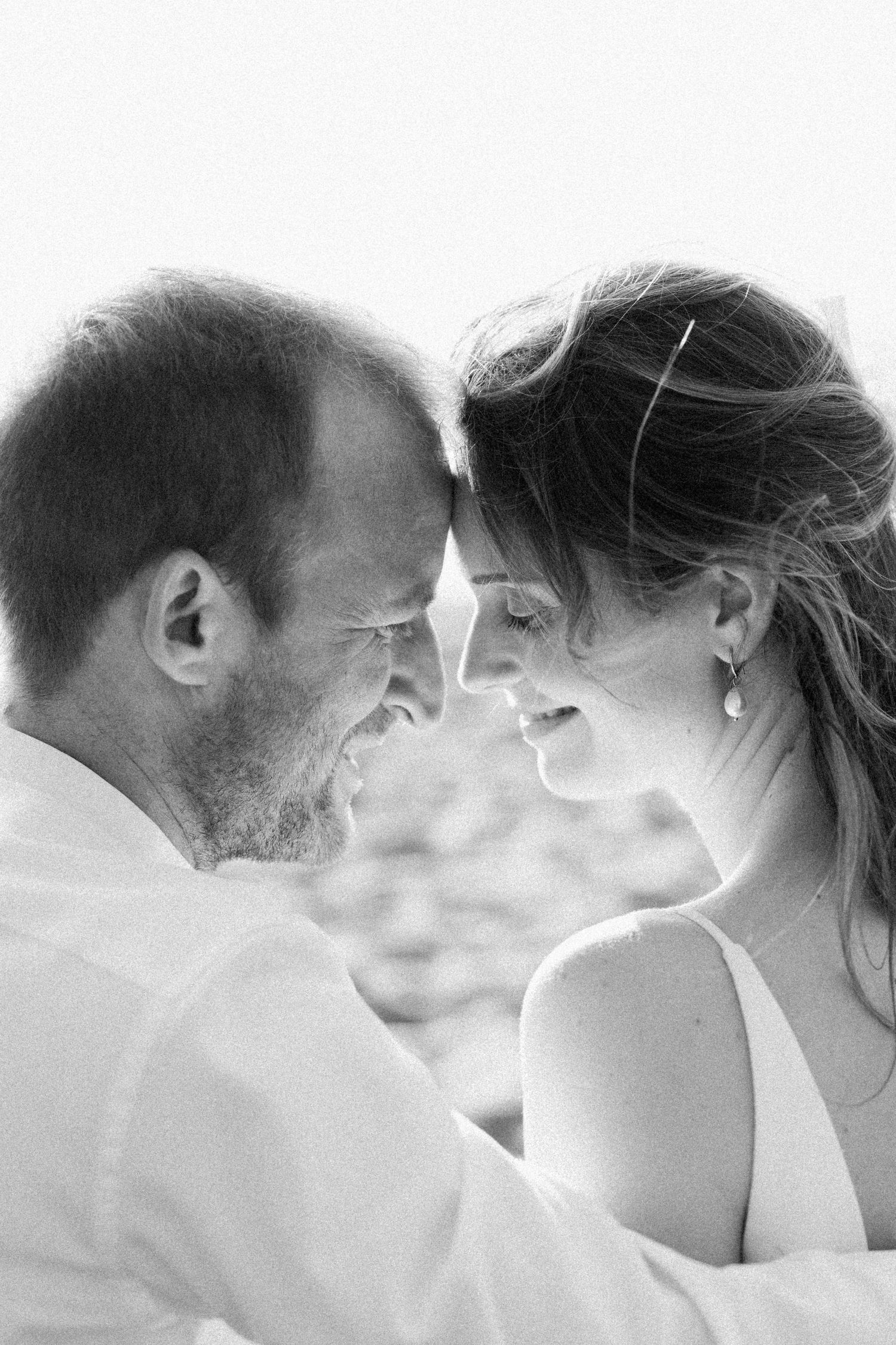 A romantic black and white portrait of a candid intimate moment between a couple, smiling at each other.