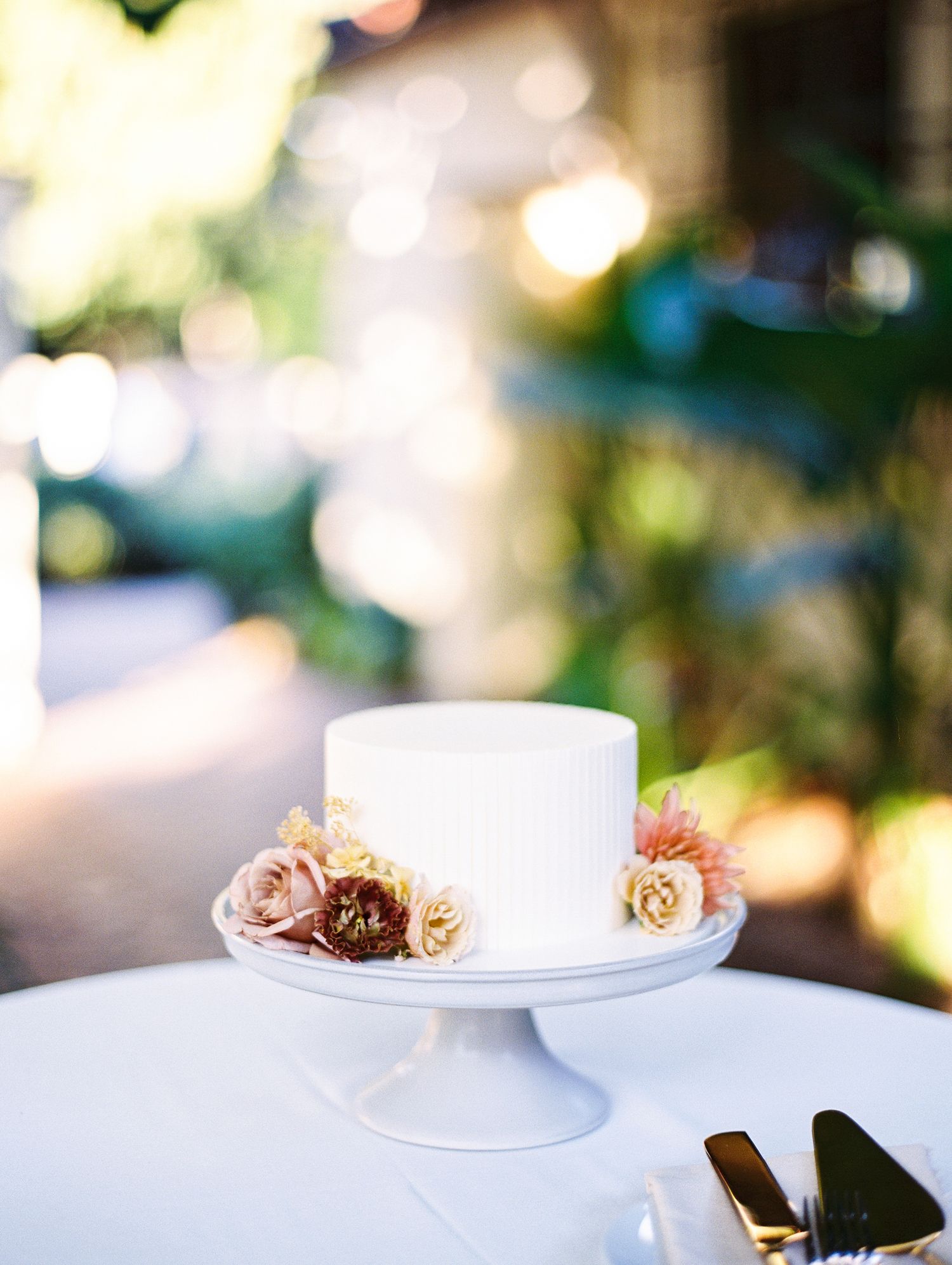 White wedding cake decorated with delicate pink and beige roses on a elegant pedestal stand.