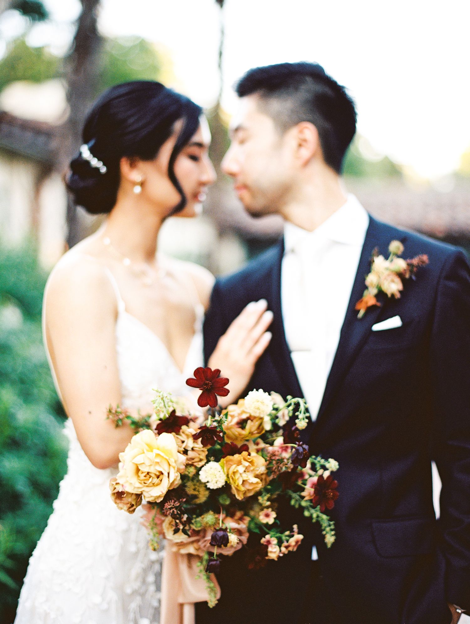 An intimate wedding portrait showing a couple with a lush autumn-toned bouquet featuring roses and peach blooms.