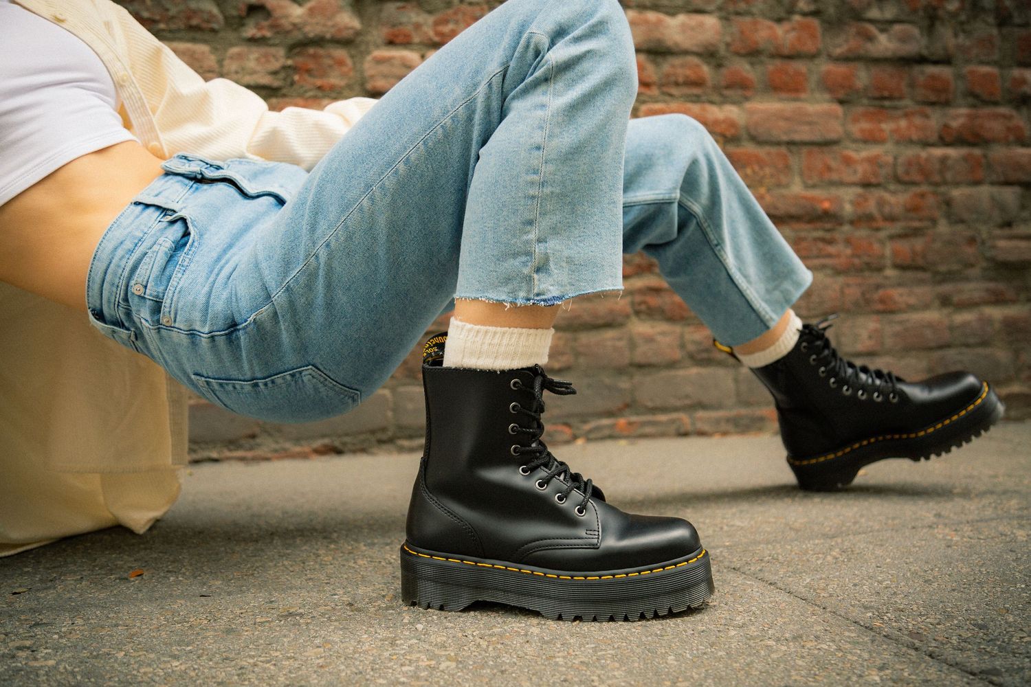 Close-up view of black leather combat boots and blue jeans against a brick wall background.