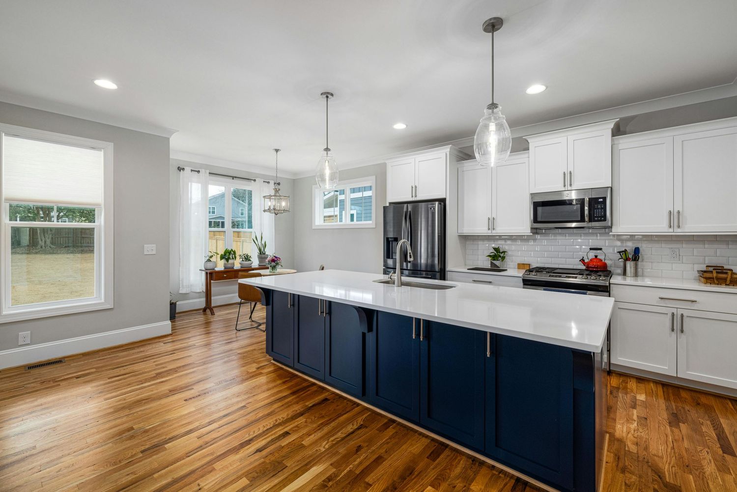 Modern kitchen with white cabinets, dark blue island, hardwood floors and pendant lighting over quartz countertops.