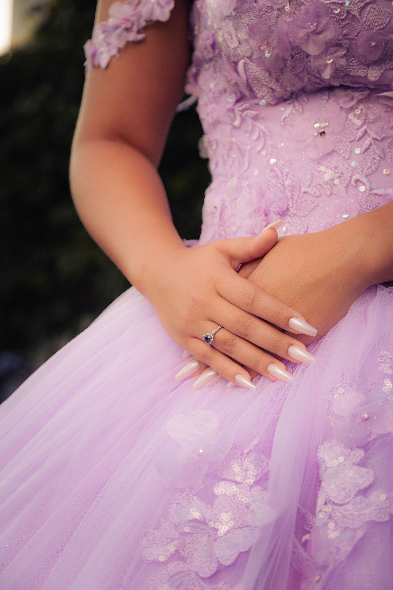 Close-up details of a lavender tulle dress with delicate floral lace embellishments and hands gracefully posed.