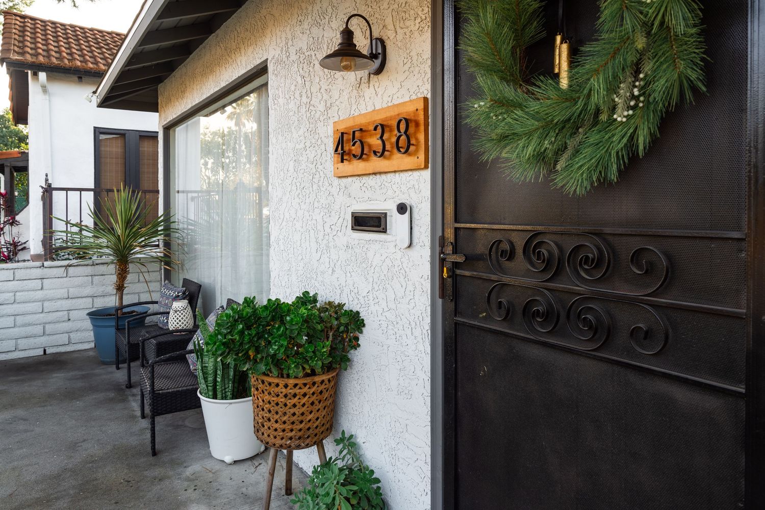 A welcoming home entrance with a black decorative door, house numbers, and potted plants on a covered porch.