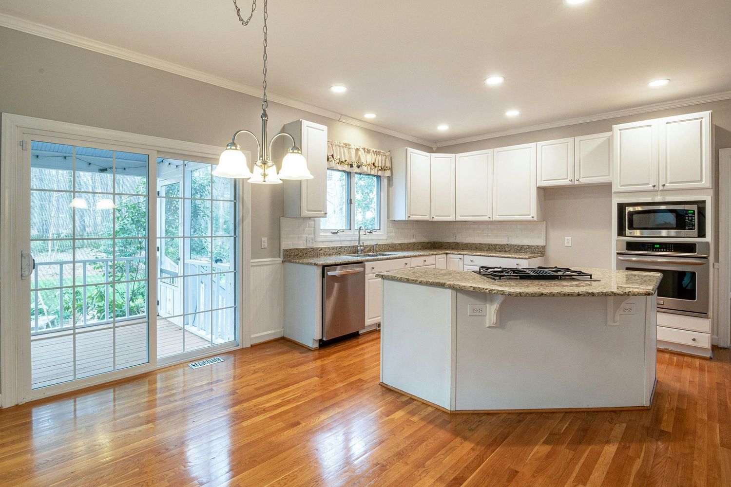 Modern open concept kitchen with white cabinets, stainless appliances, and hardwood floors extends into bright living space.