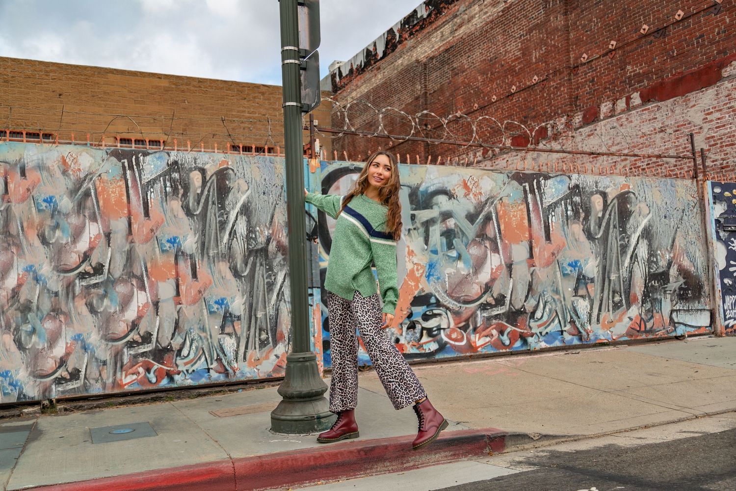 A long wall covered in colorful graffiti art stretches along an urban street with brick buildings in the background.