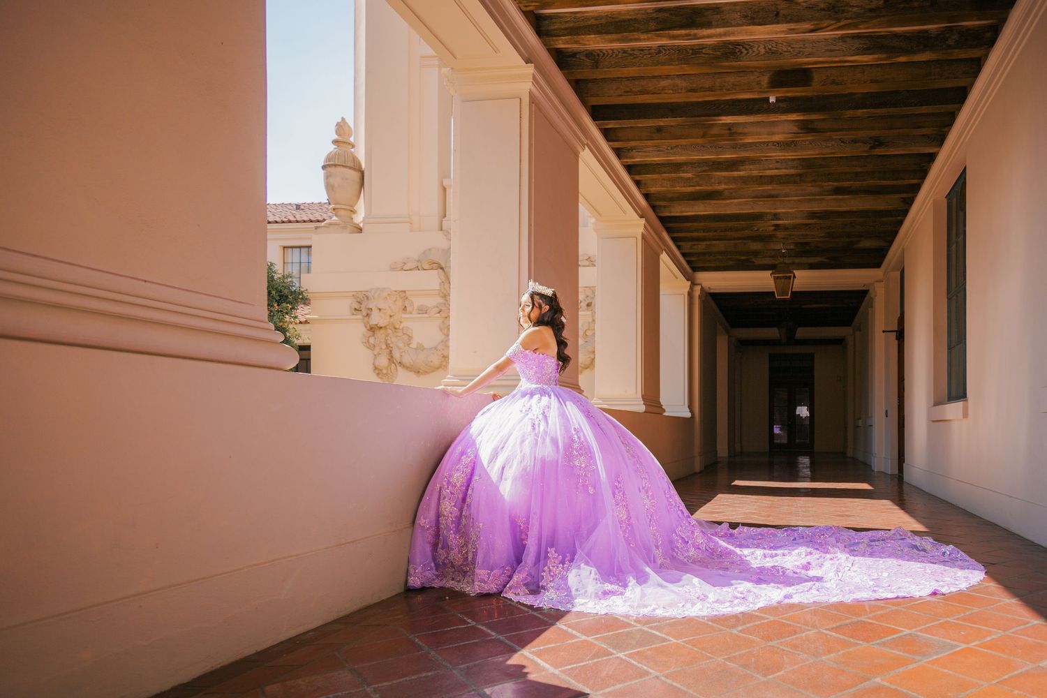A person in a flowing pink ballgown poses in different positions along a hallway with wooden beams and white walls.