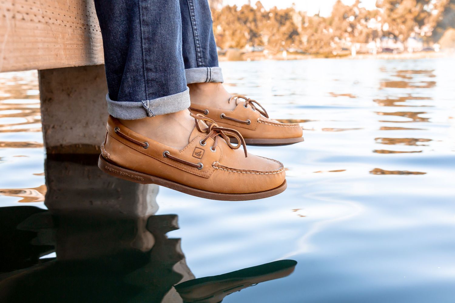Brown leather boat shoes worn on dock with water reflections at sunset.
