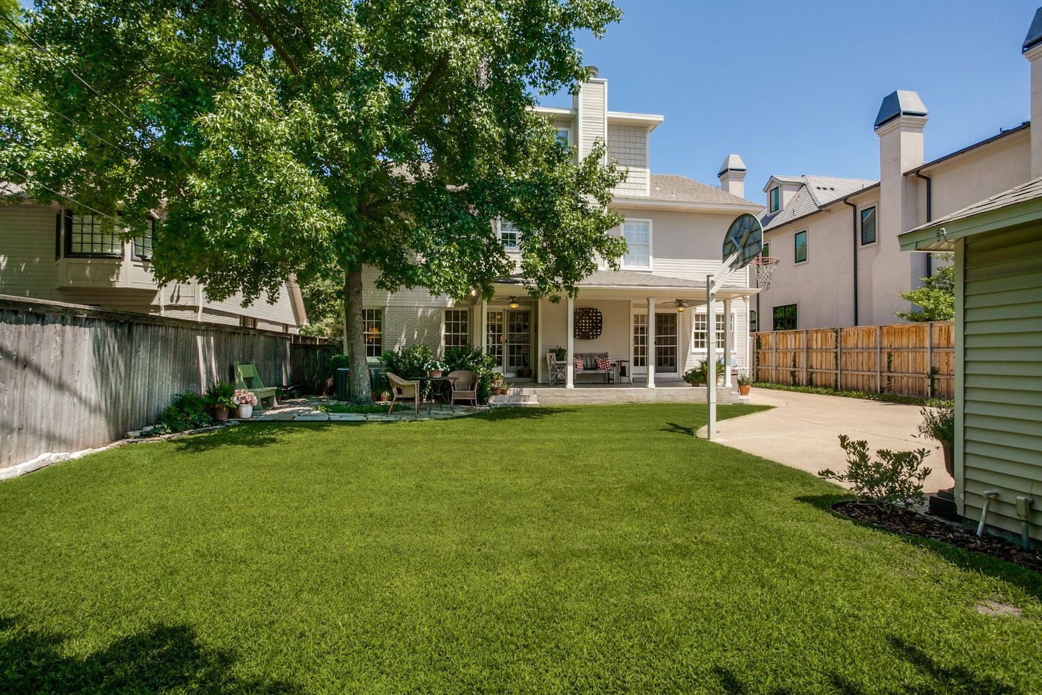 Large backyard with lush green lawn surrounded by residential houses and mature trees.