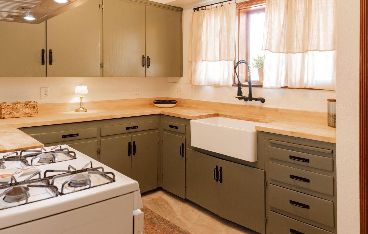 Panoramic view of a modern kitchen interior with butcher block countertops and olive green cabinets.