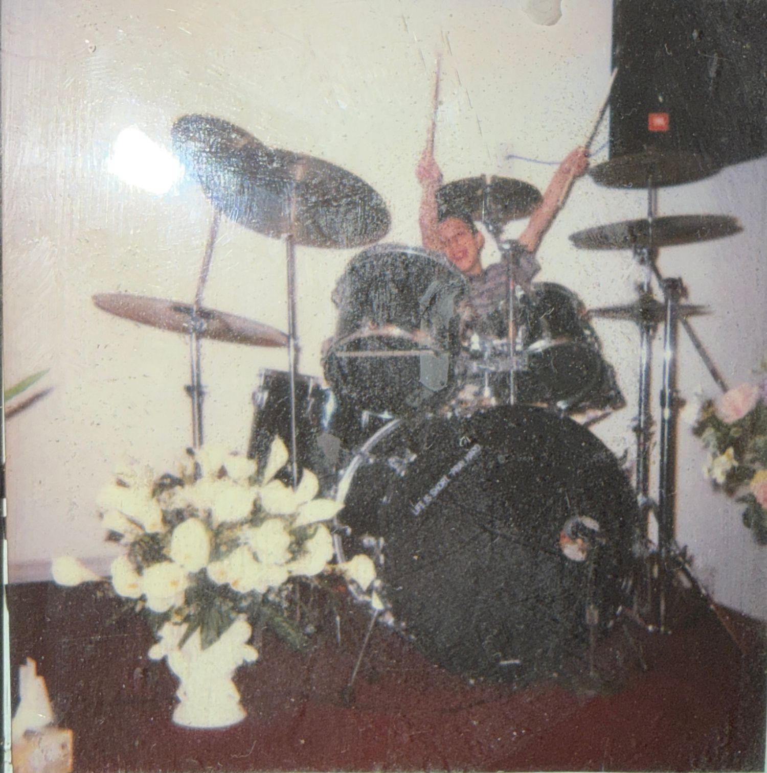 Panoramic view of a drum kit on stage with white floral decorations visible in multiple segments.