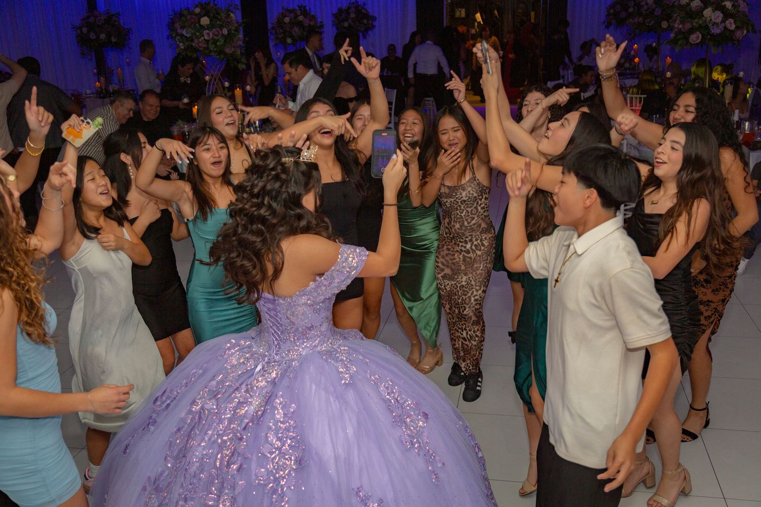 A crowded dance floor filled with people dancing and celebrating at a formal event with a person in a purple gown.