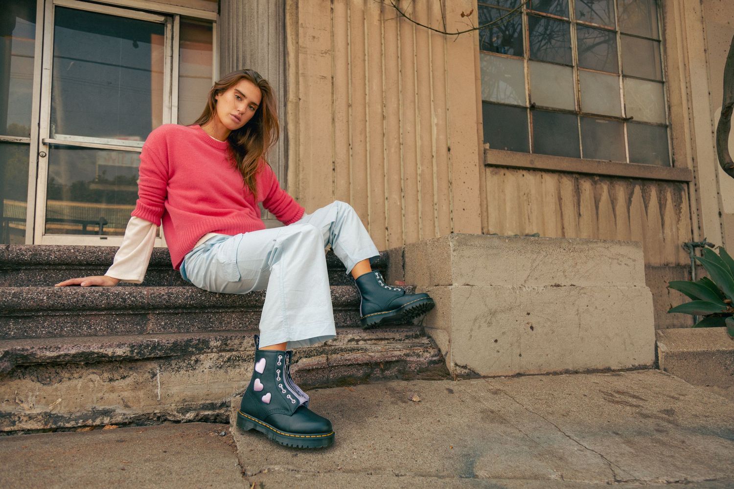A person in a pink sweater and jeans sits on wooden steps in a casual outdoor photo shoot series.