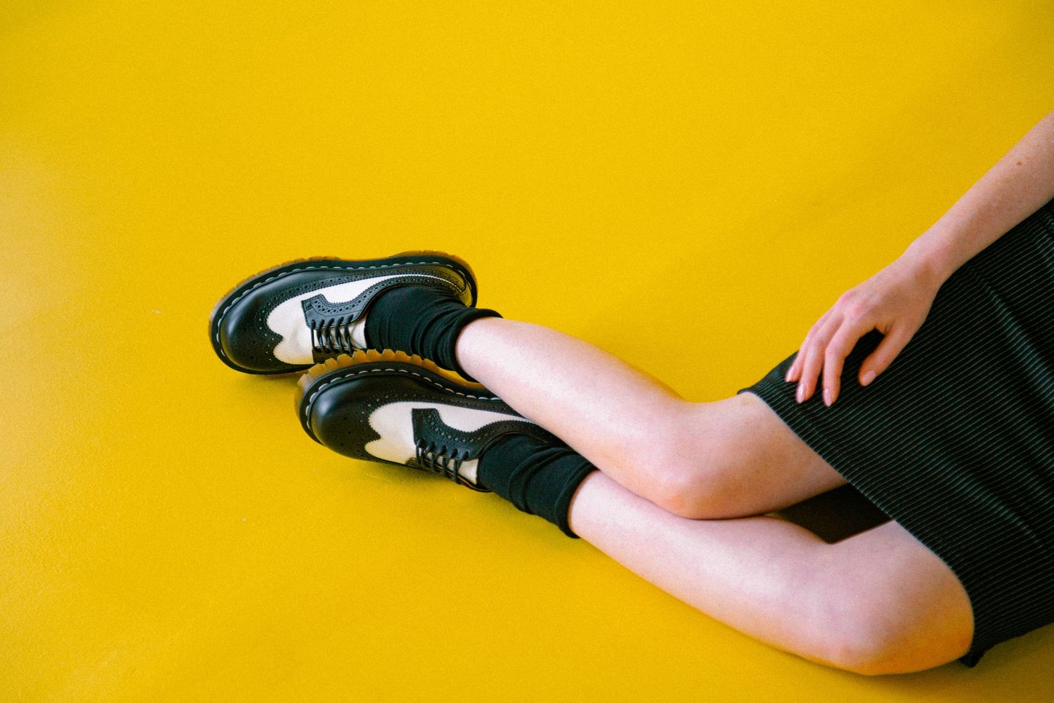 Person wearing black sneakers with white soles sits on yellow background in a sequence of leg positions.