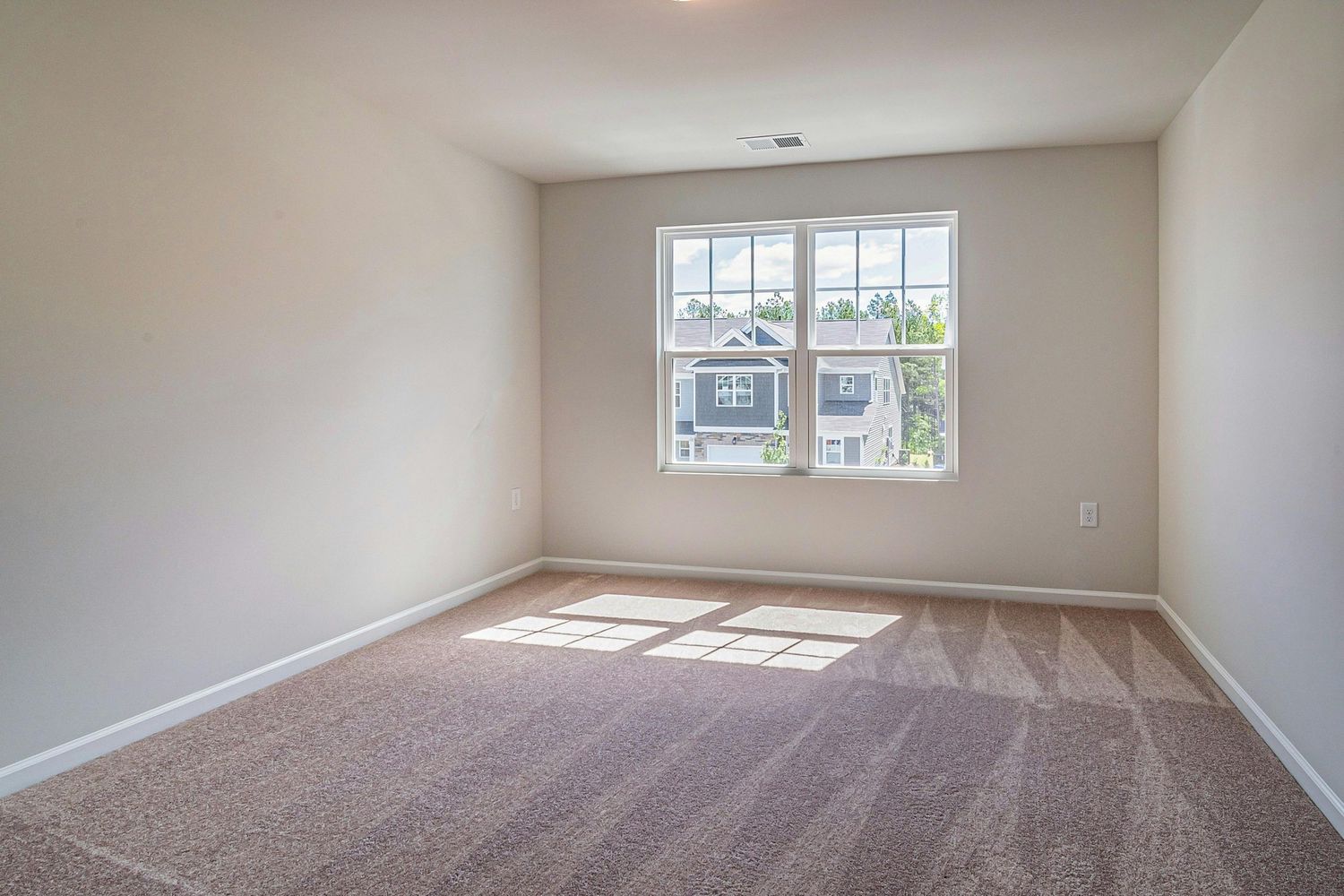 Empty beige bedroom with large windows letting in natural light and beige carpet flooring.