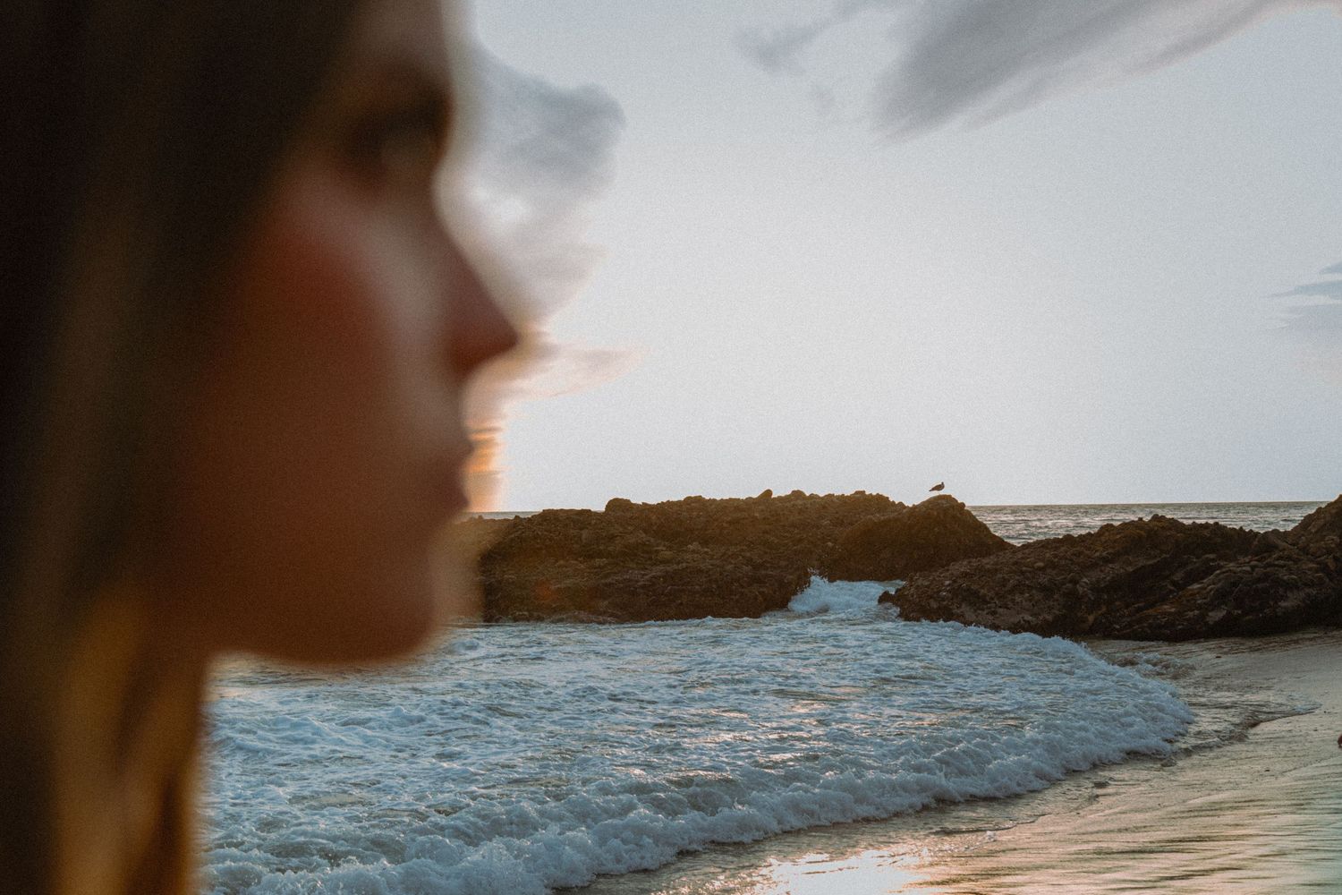 Blurred silhouette against a coastal seascape with rocky cliffs and ocean waves at sunset.