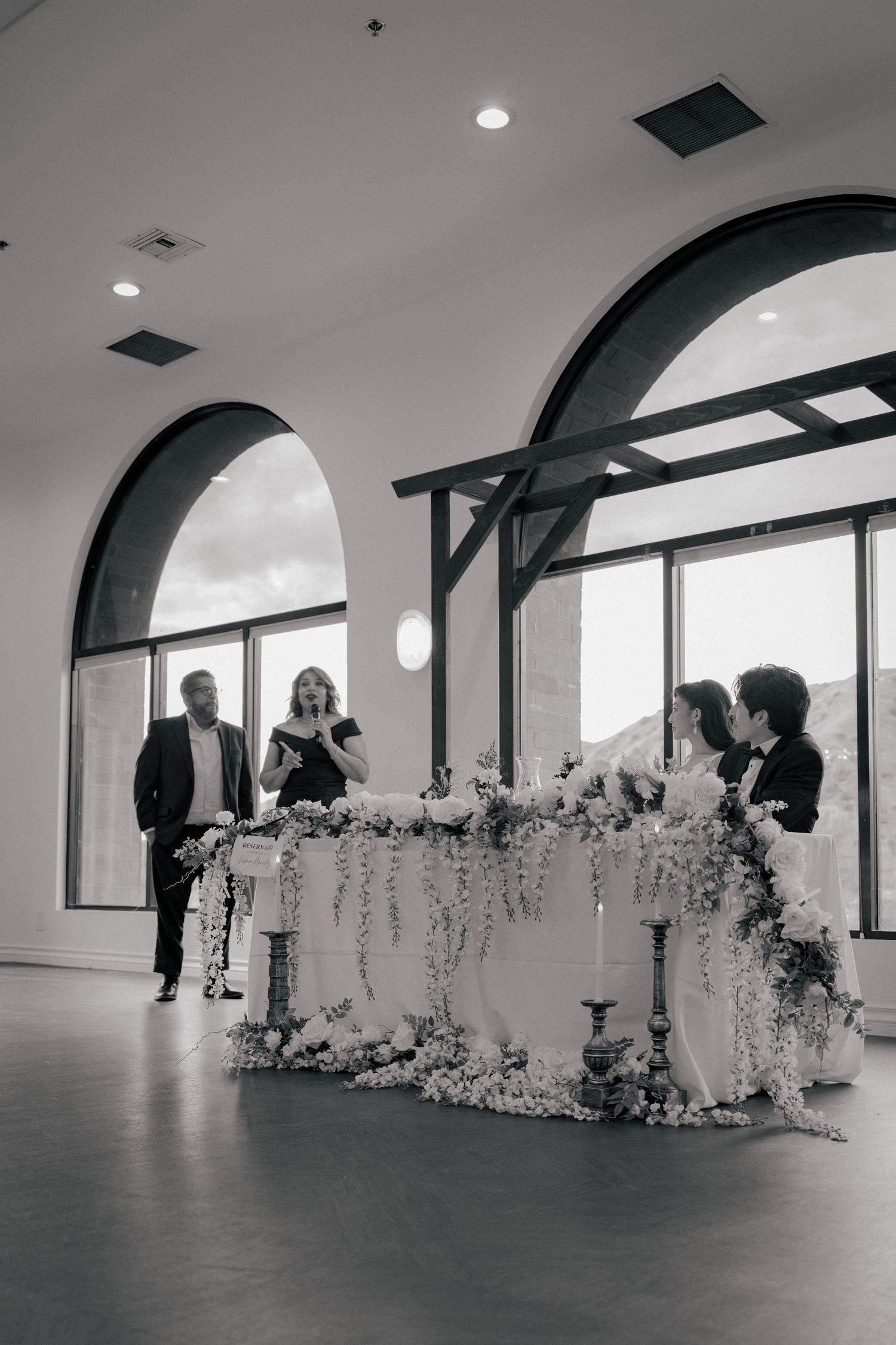A series of black and white photos showing a long banquet table decorated with white floral arrangements in an elegant venue.