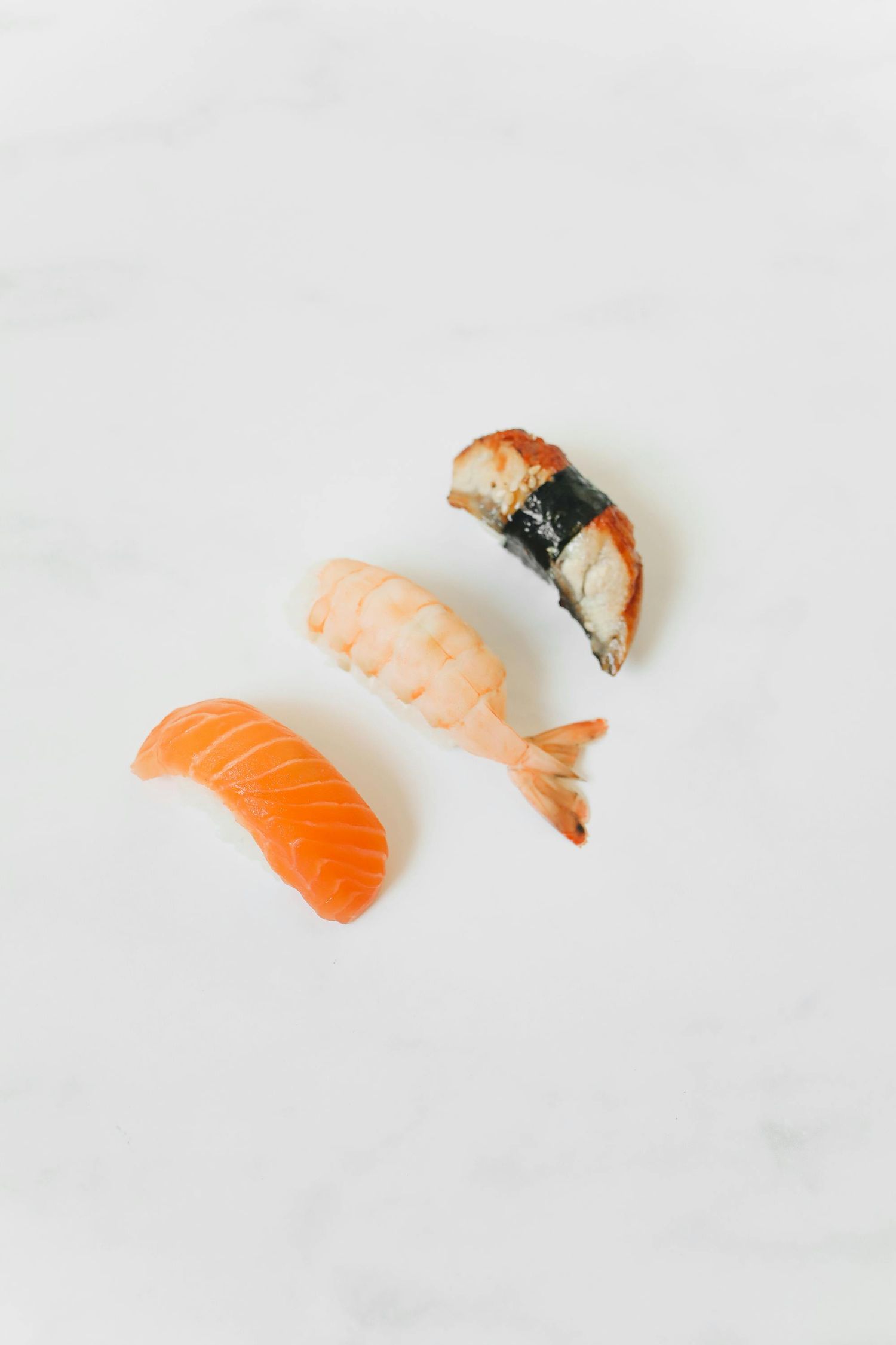 Four pieces of fresh nigiri sushi with salmon and shrimp arranged in a row on white marble background.