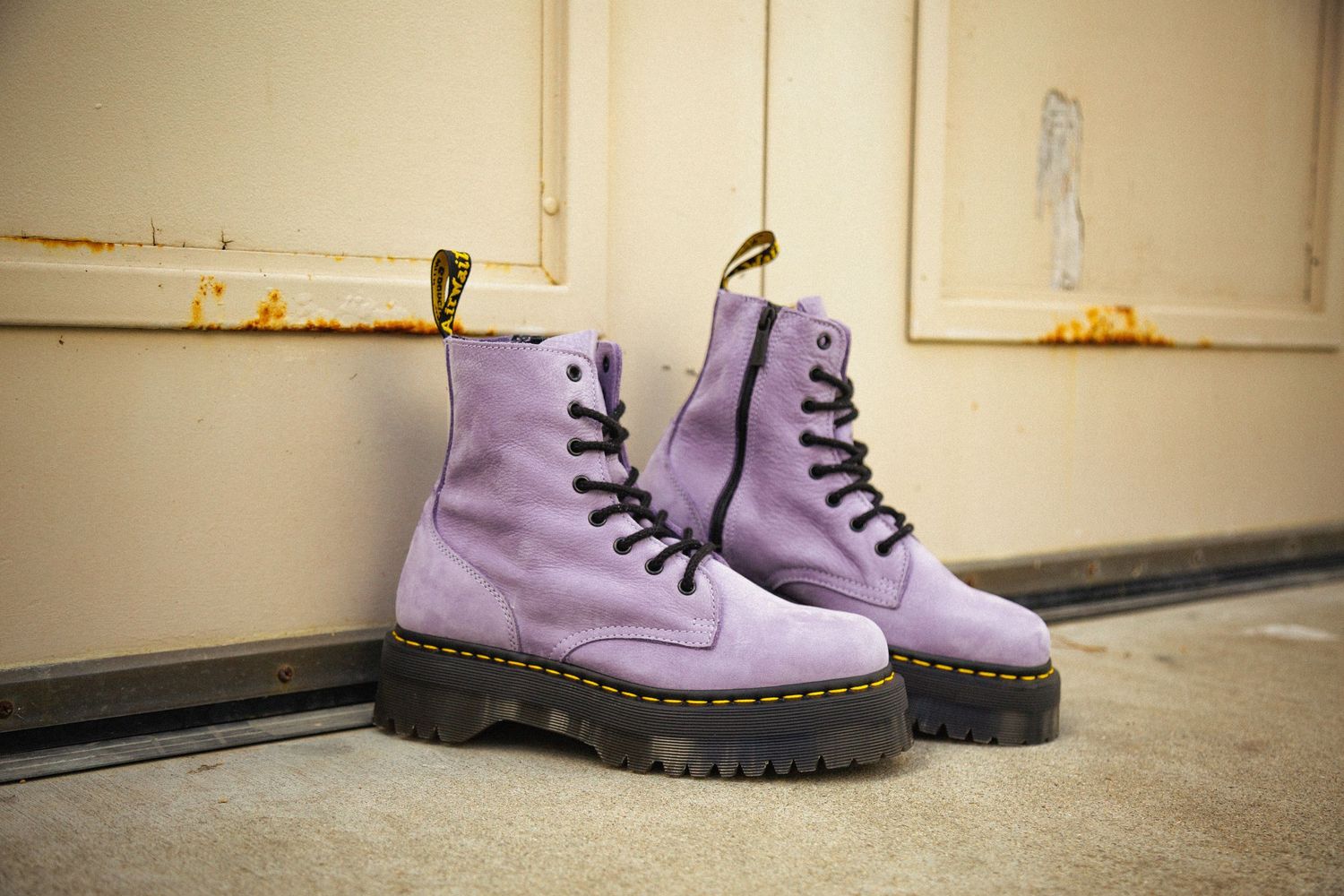 A pair of pastel purple combat boots with black laces and chunky soles shown from multiple angles on a light floor.