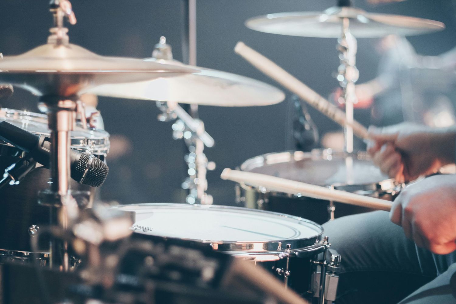 Close-up view of a drummer performing on a professional drum kit with cymbals in moody lighting.