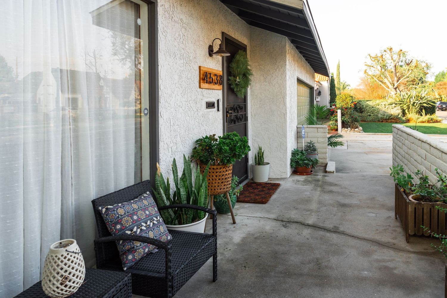Cozy front porch with a black bench, potted plants, and decorative lantern against white stucco exterior at sunset.
