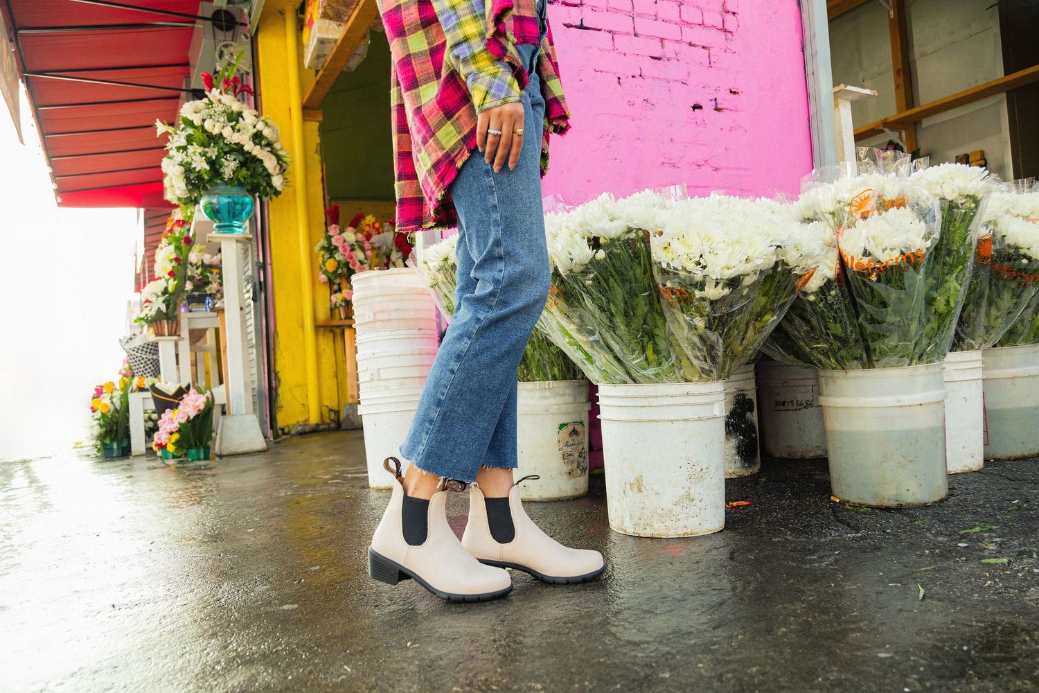 Colorful storefront displays with white buckets and pink brick walls showing someone's legs and feet walking by.
