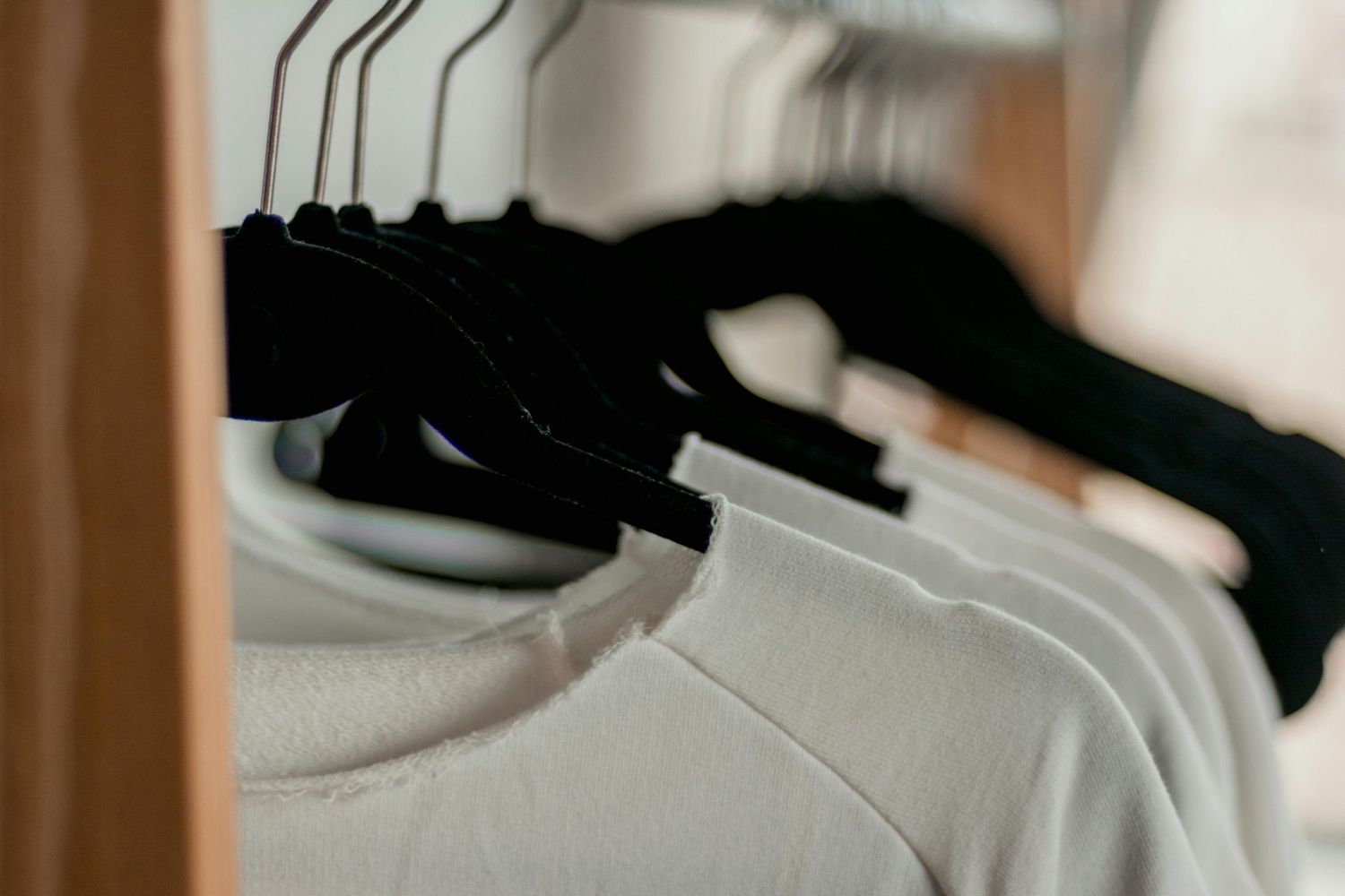 Row of white and black t-shirts hanging on velvet hangers in a closet shown in shallow focus.